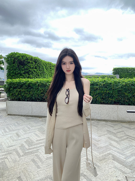 Woman wearing a beige outfit with a cardigan and holding sunglasses.