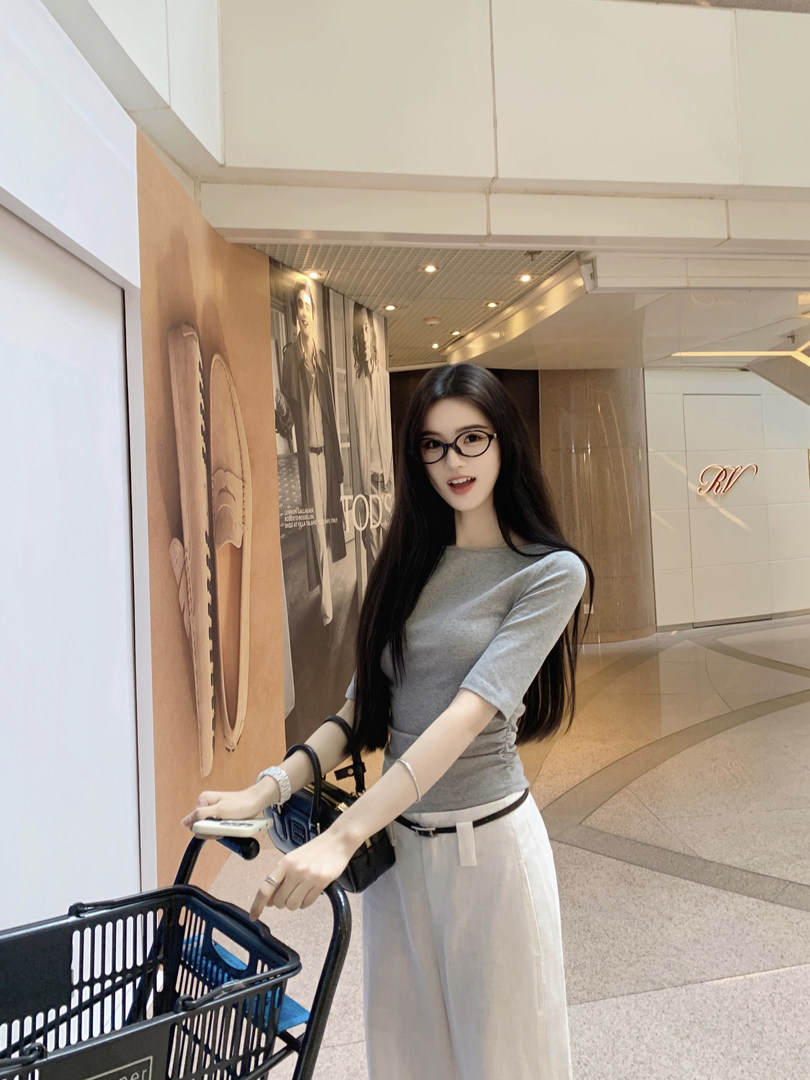 Woman wearing a gray top and white pants, posing with a shopping cart in a mall.