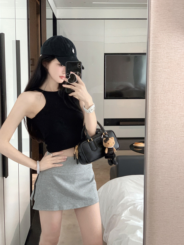 Woman wearing a black sleeveless crop top and gray mini skirt with a black handbag