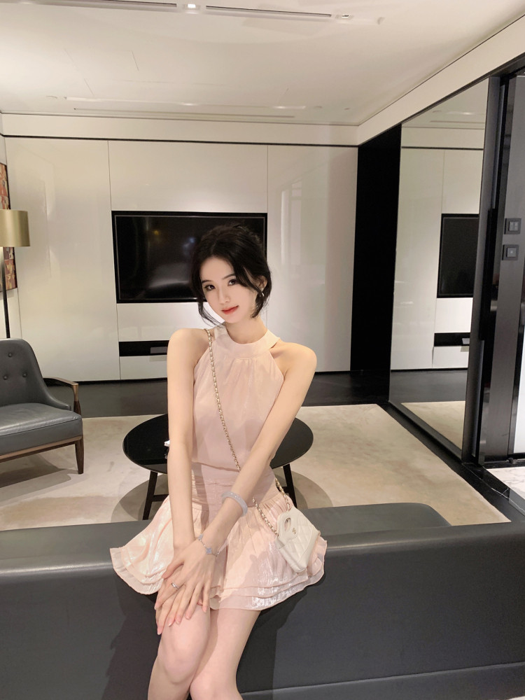 Woman wearing a light pink sleeveless dress with ruffled hem, sitting on a sofa in a modern living room
