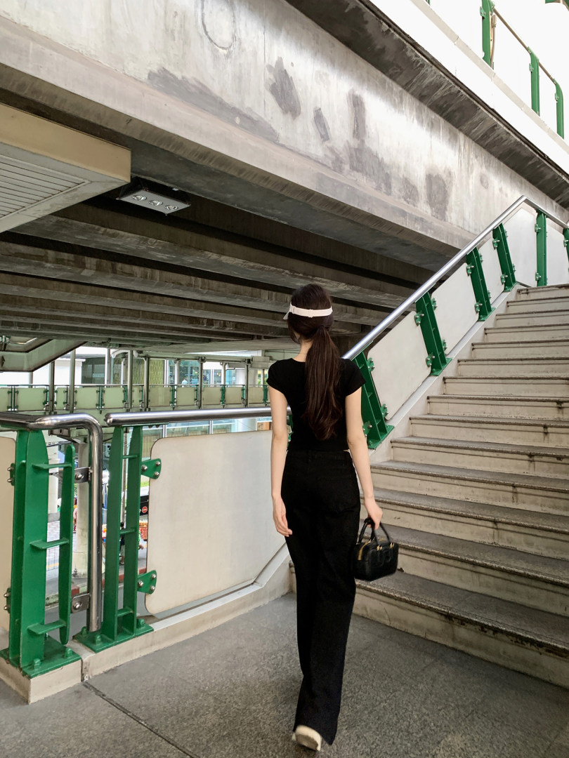 Woman wearing black top and pants walking on stairs, carrying small black handbag