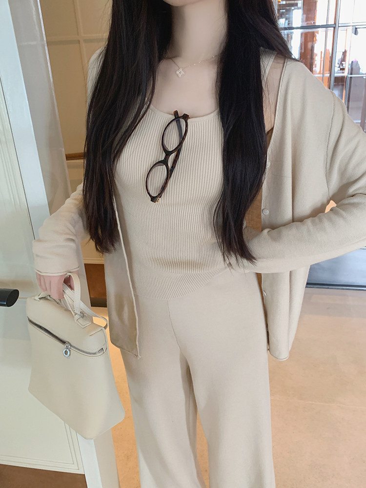 Woman wearing beige ribbed tank top, matching cardigan and pants, holding handbag with glasses on chest