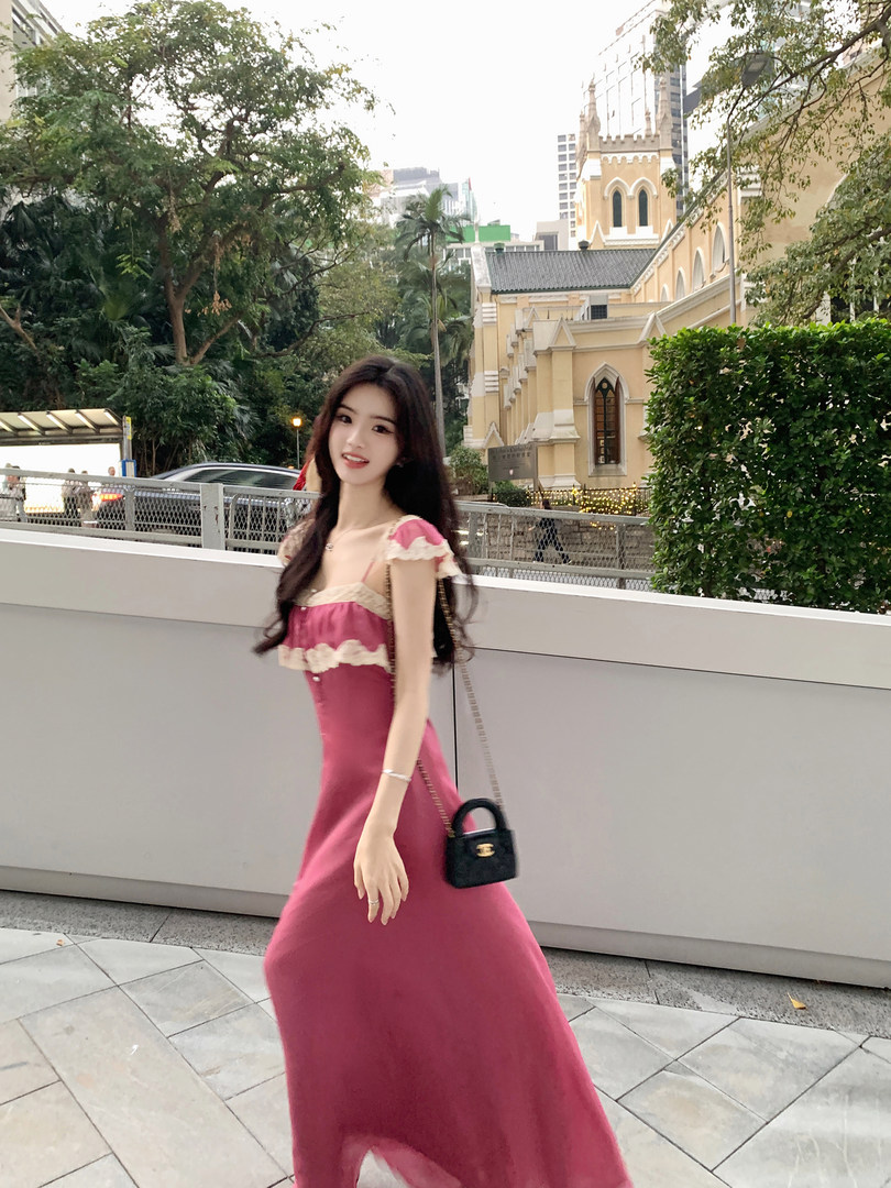 Woman wearing a pink dress with lace details, standing outdoors near a building.
