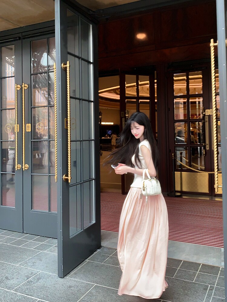Woman wearing a pink satin dress and holding a white handbag outside a building with glass doors.