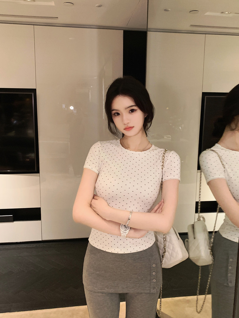 Woman wearing white polka dot short-sleeve top and gray skirt with buttons, carrying white chain bag