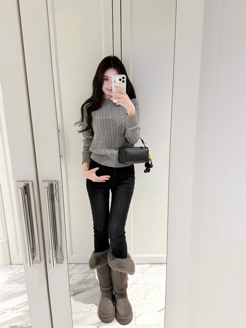 Woman taking mirror selfie wearing gray cable knit sweater, black jeans, and gray fur-trimmed boots