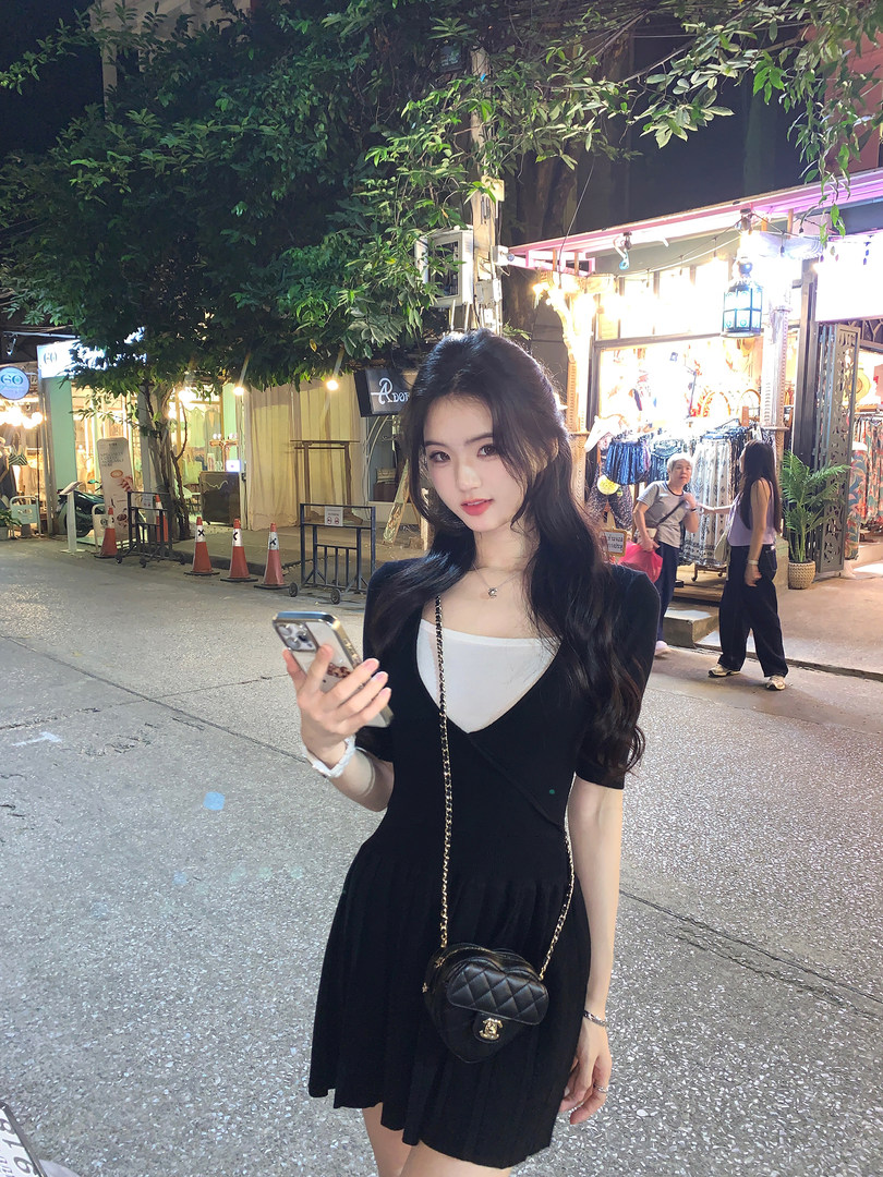 Woman wearing a black pleated dress with white inner layer, holding phone, outdoors at night