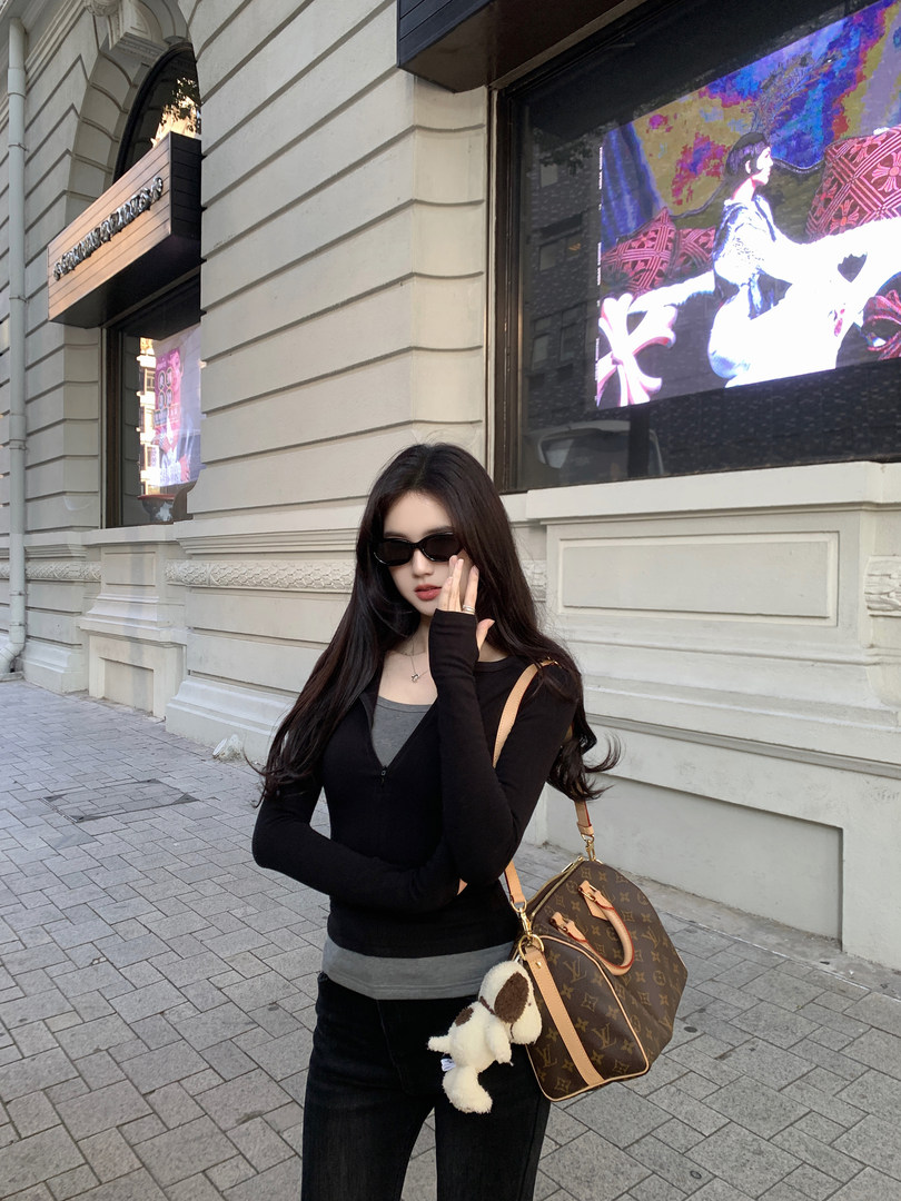 Woman wearing black long-sleeve top and carrying a brown monogram handbag on a city street.
