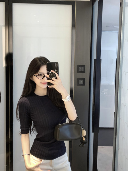 Woman taking mirror selfie wearing black ribbed top and white pants with a black bag.