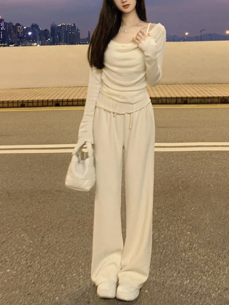Woman wearing a white long-sleeve top and matching wide-leg pants with a white handbag, standing on a street at dusk.