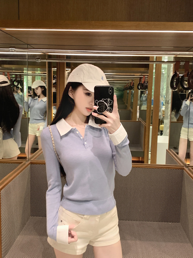 Woman taking mirror selfie wearing light blue long-sleeve polo top with white collar and cream shorts
