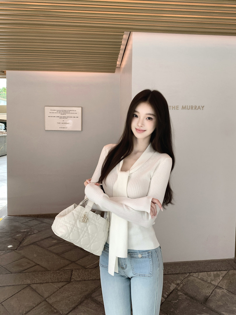 Woman wearing a white ribbed cardigan and light blue jeans, holding a white quilted handbag