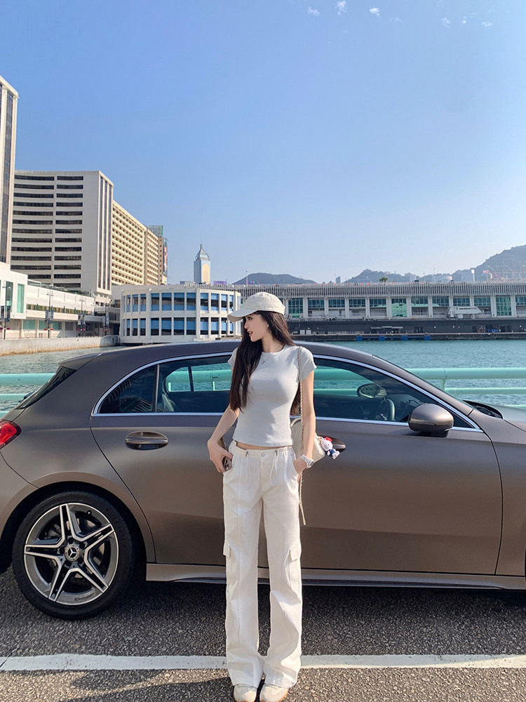 Woman wearing white outfit standing next to a car with cityscape background