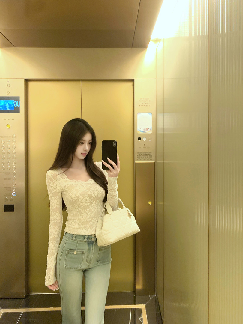 Woman taking mirror selfie in elevator wearing lace top and jeans with handbag