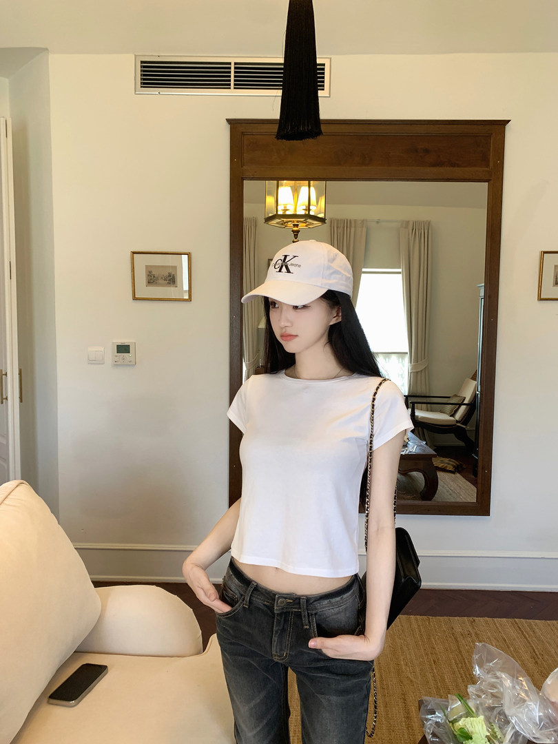 Woman wearing white crop top, jeans, and a white cap with CK logo