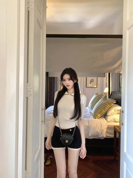 Woman wearing white knit top and black lace-trim shorts with heart-shaped bag, standing in doorway