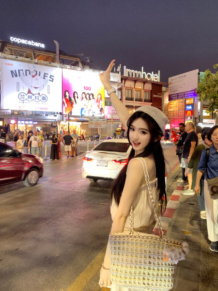 Woman wearing white top and carrying woven handbag on busy city street at night