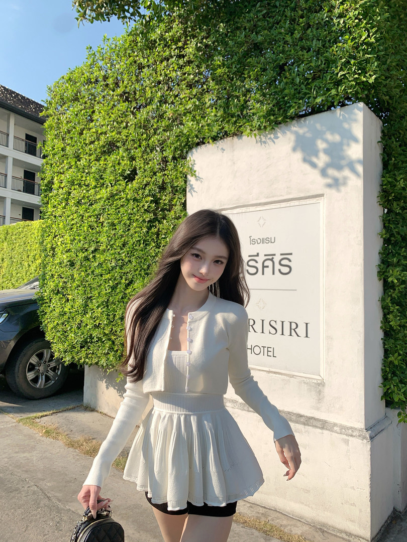 Woman wearing a white knitted cardigan and matching skirt in front of a hotel sign