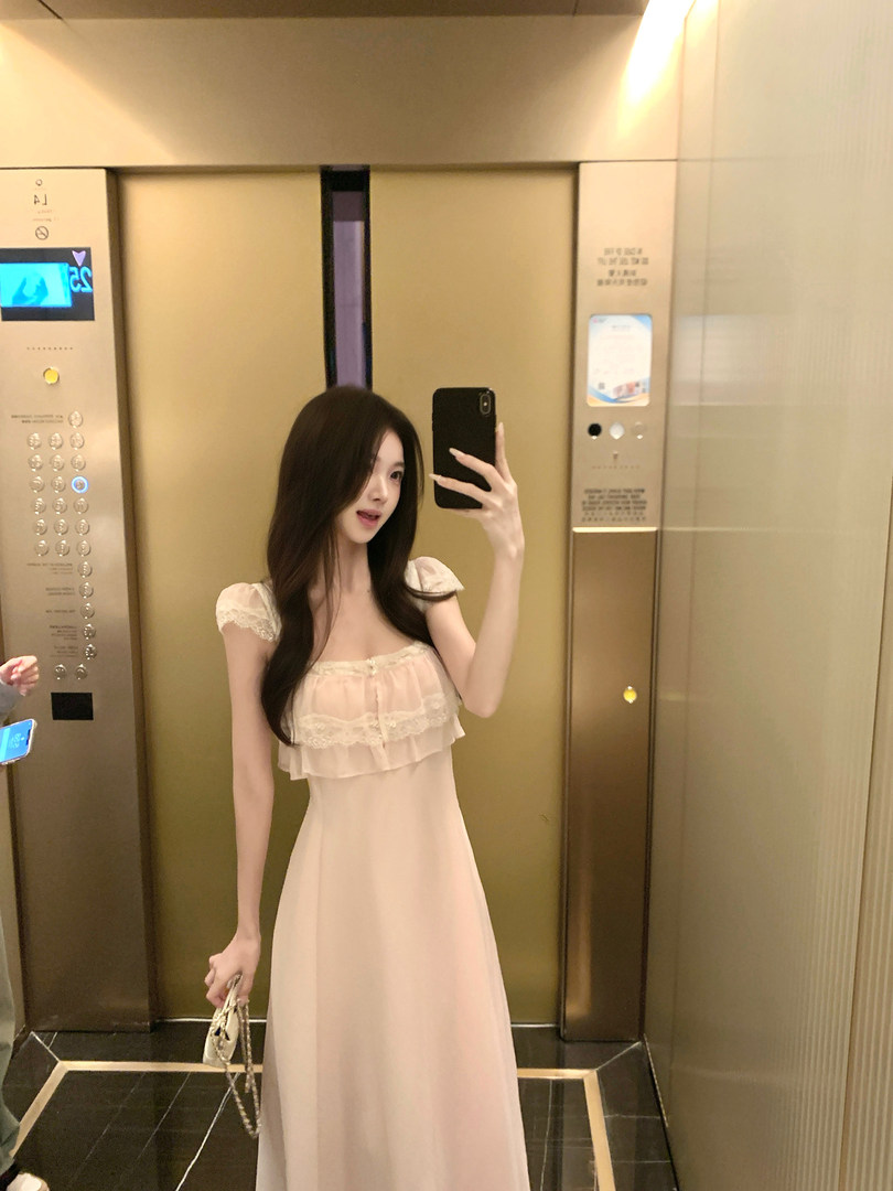 Woman taking a mirror selfie in an elevator wearing a light pink lace dress