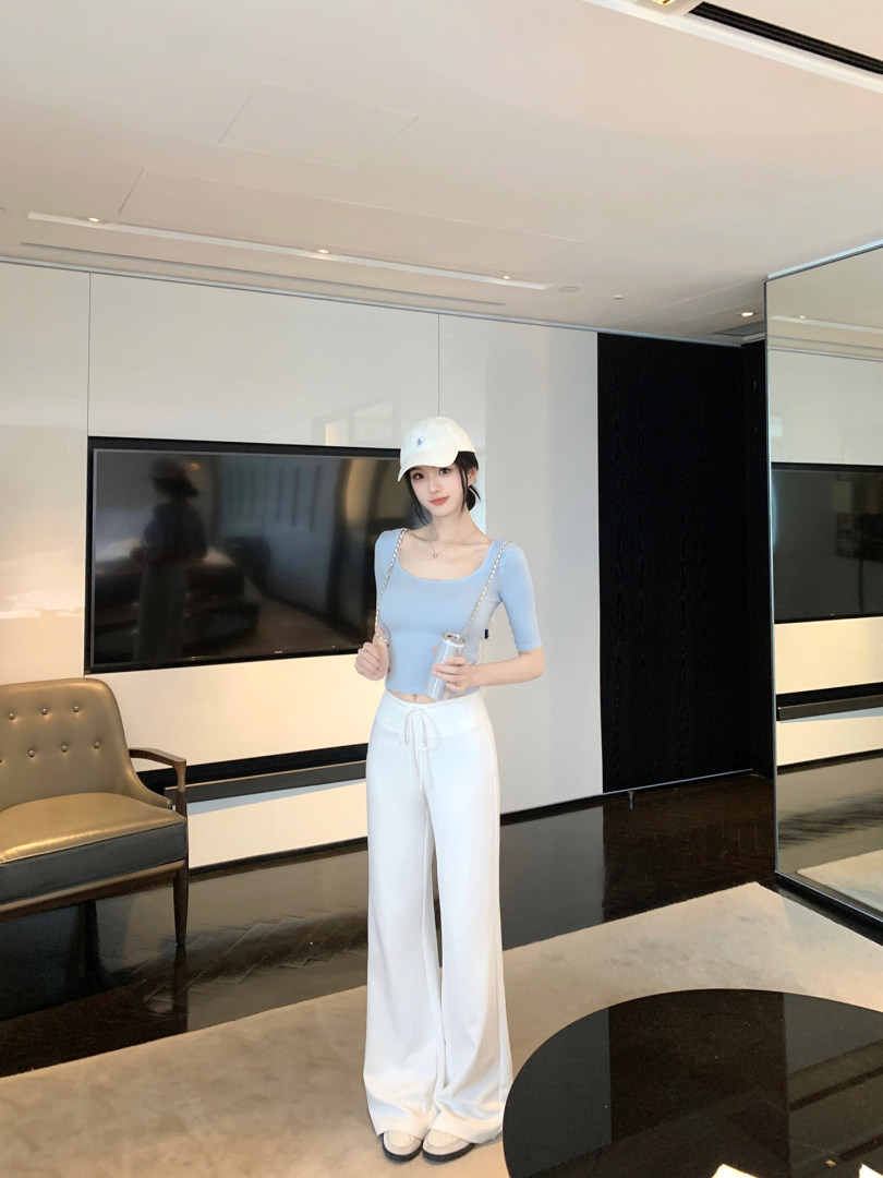 Woman wearing light blue crop top and white wide-leg pants in a modern indoor setting