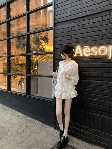 Woman wearing white ruffled outfit standing against a brick wall with neon sign