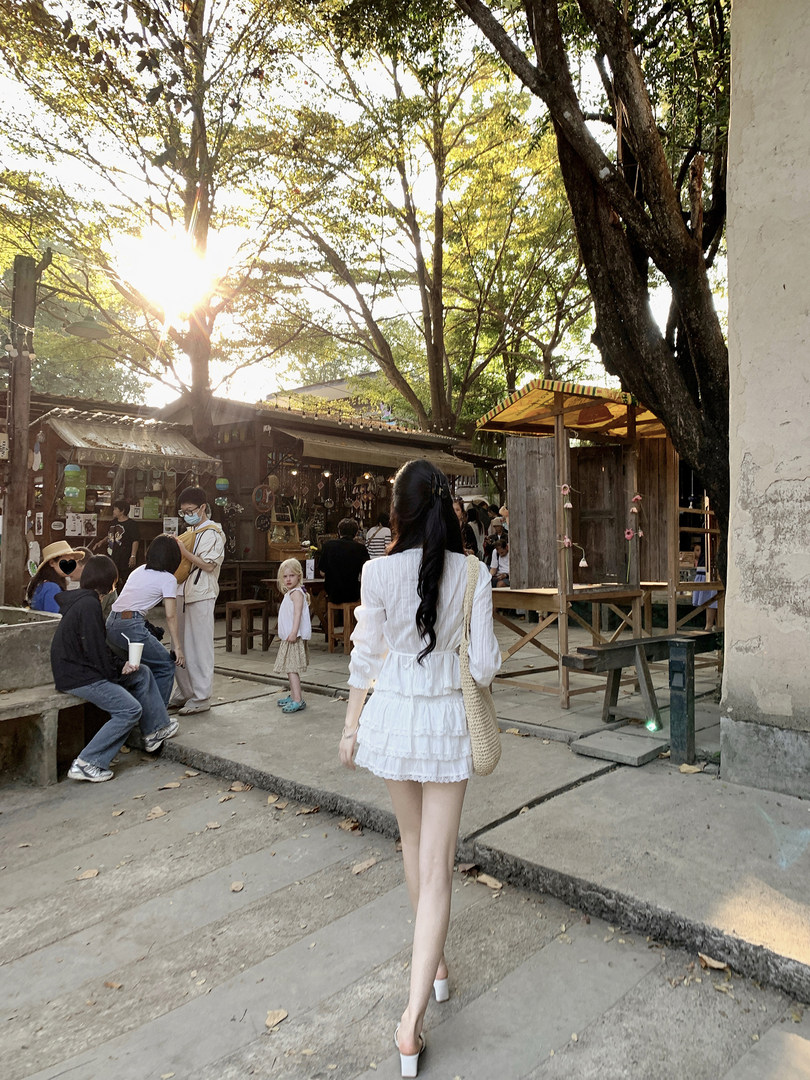 Woman wearing a white tiered dress walking outdoors in a market area