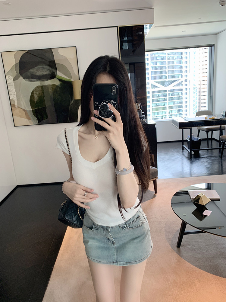 Woman taking mirror selfie wearing white top and denim skirt