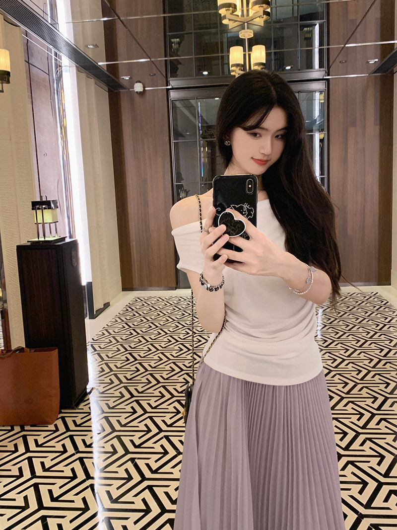 Woman taking mirror selfie wearing white off-shoulder top and pleated skirt