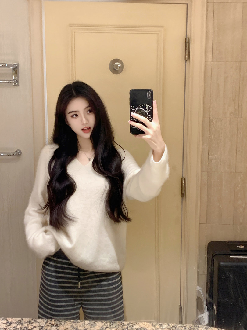 Woman taking mirror selfie wearing white V-neck sweater and striped pants
