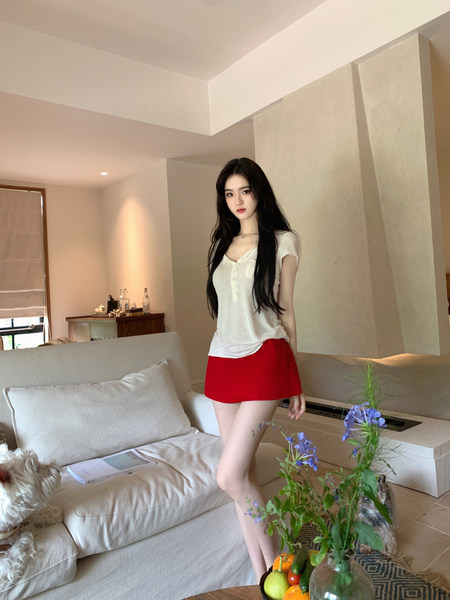 Woman wearing white short-sleeve top and red mini skirt in a modern living room setting