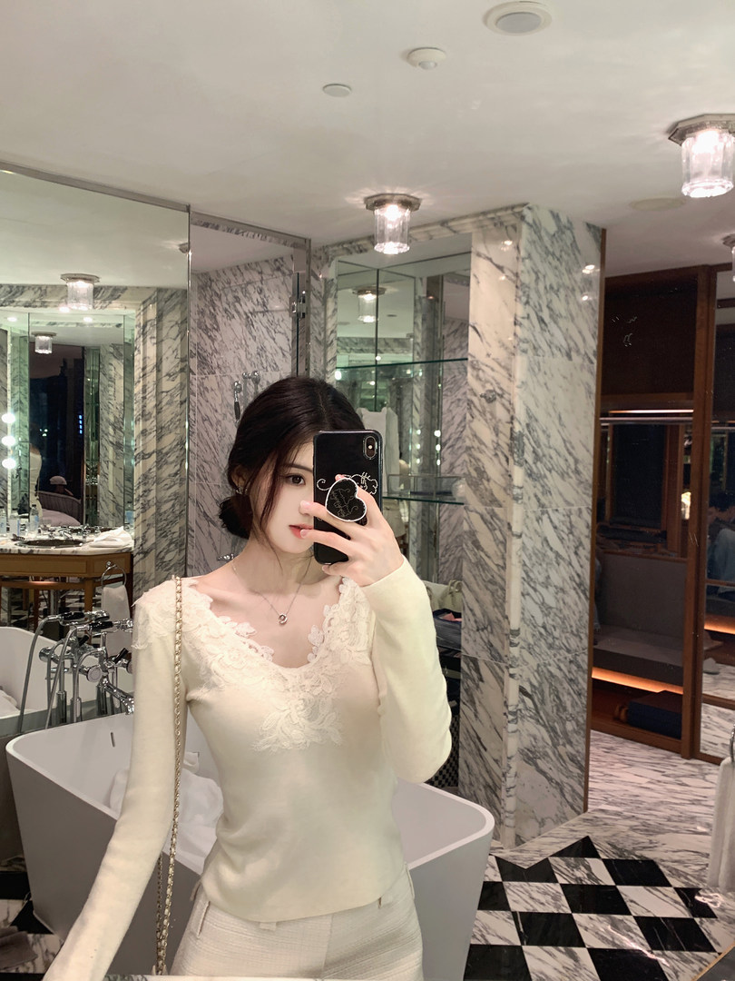 Woman taking mirror selfie wearing white lace top and matching pants in a luxurious bathroom
