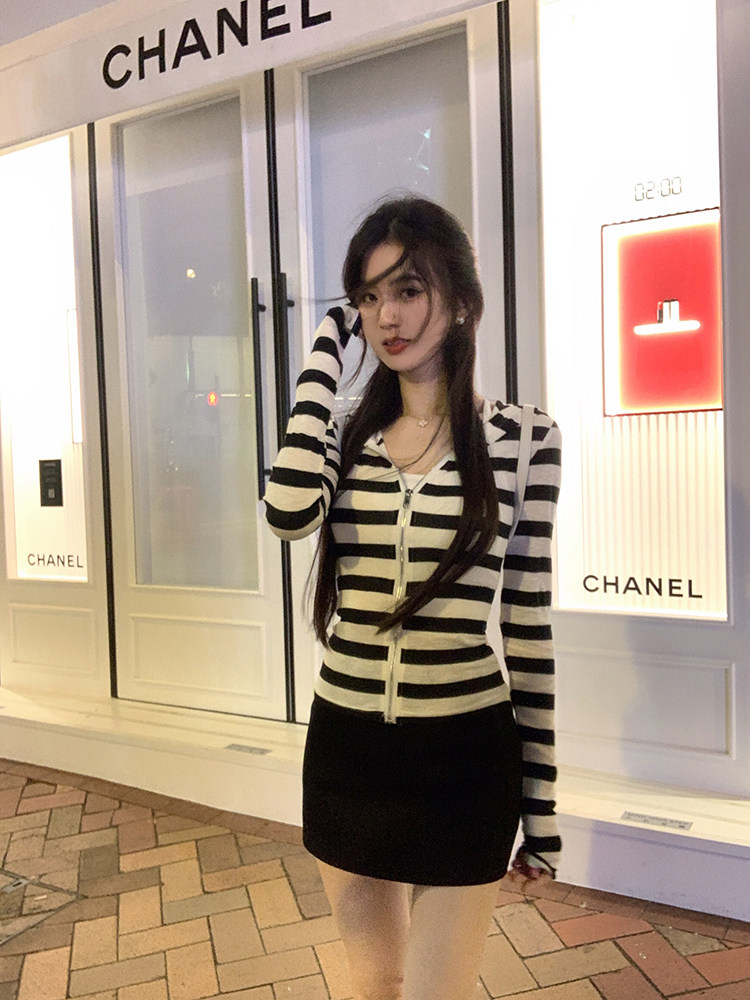 Woman wearing black and white striped zip-up cardigan and black mini skirt in front of Chanel store
