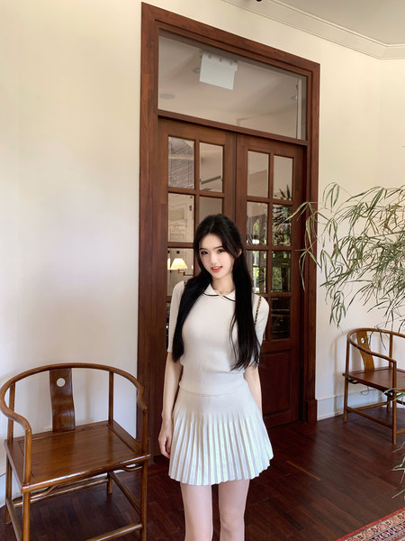 Woman wearing a white ribbed top and pleated skirt standing indoors