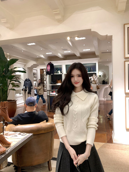 Woman wearing a cream cable-knit sweater with a Peter Pan collar in a store setting