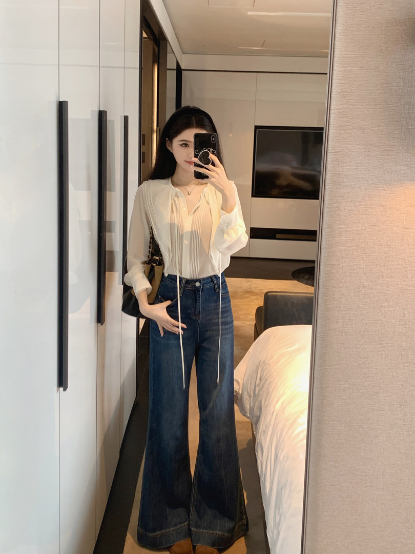 Woman taking mirror selfie wearing white blouse and wide-leg jeans