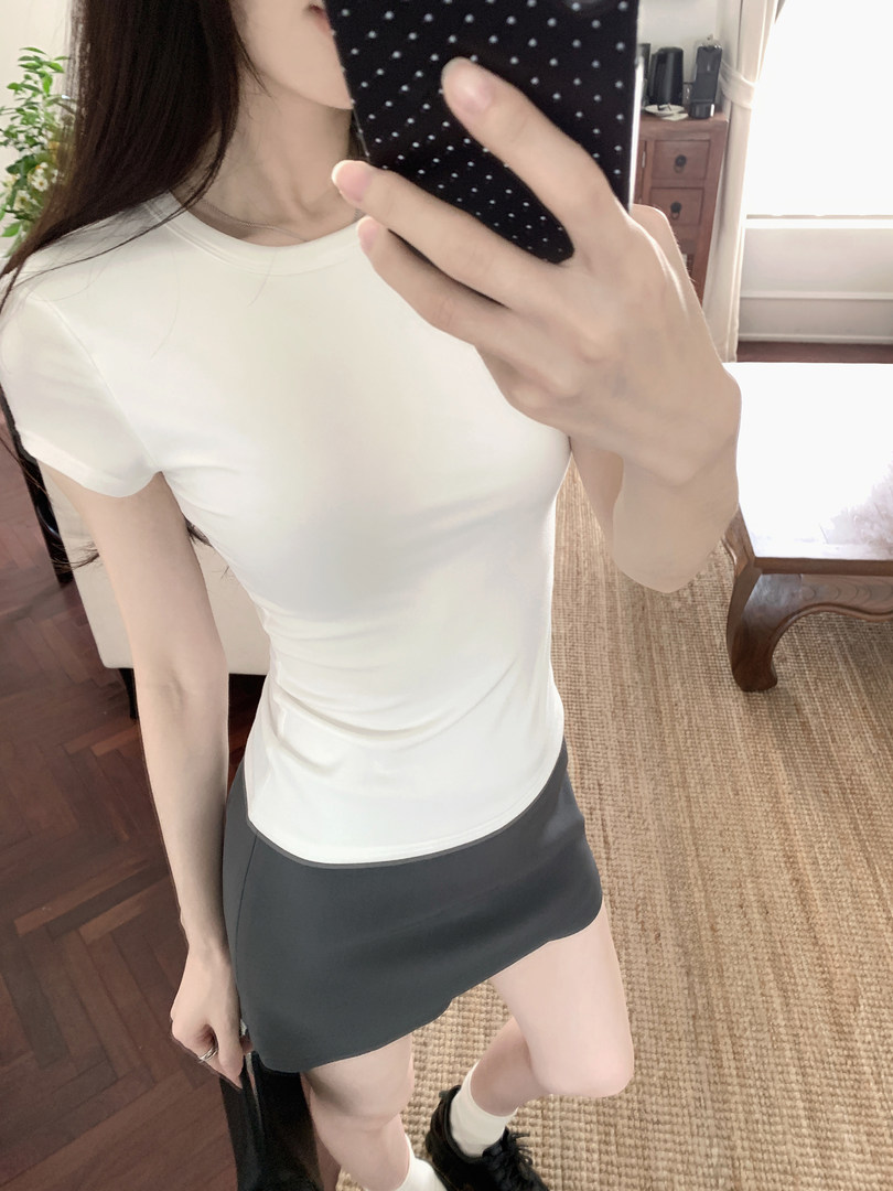Woman wearing a white fitted t-shirt and black mini skirt, taking a mirror selfie