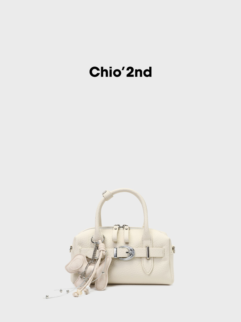 Cream leather handbag with charm accessory on a plain background