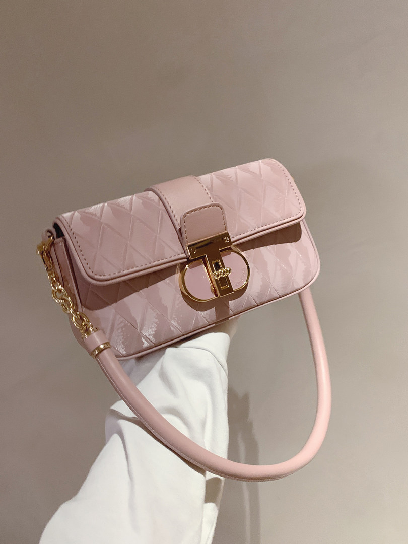Pink quilted handbag with gold chain and clasp detail being held in hand