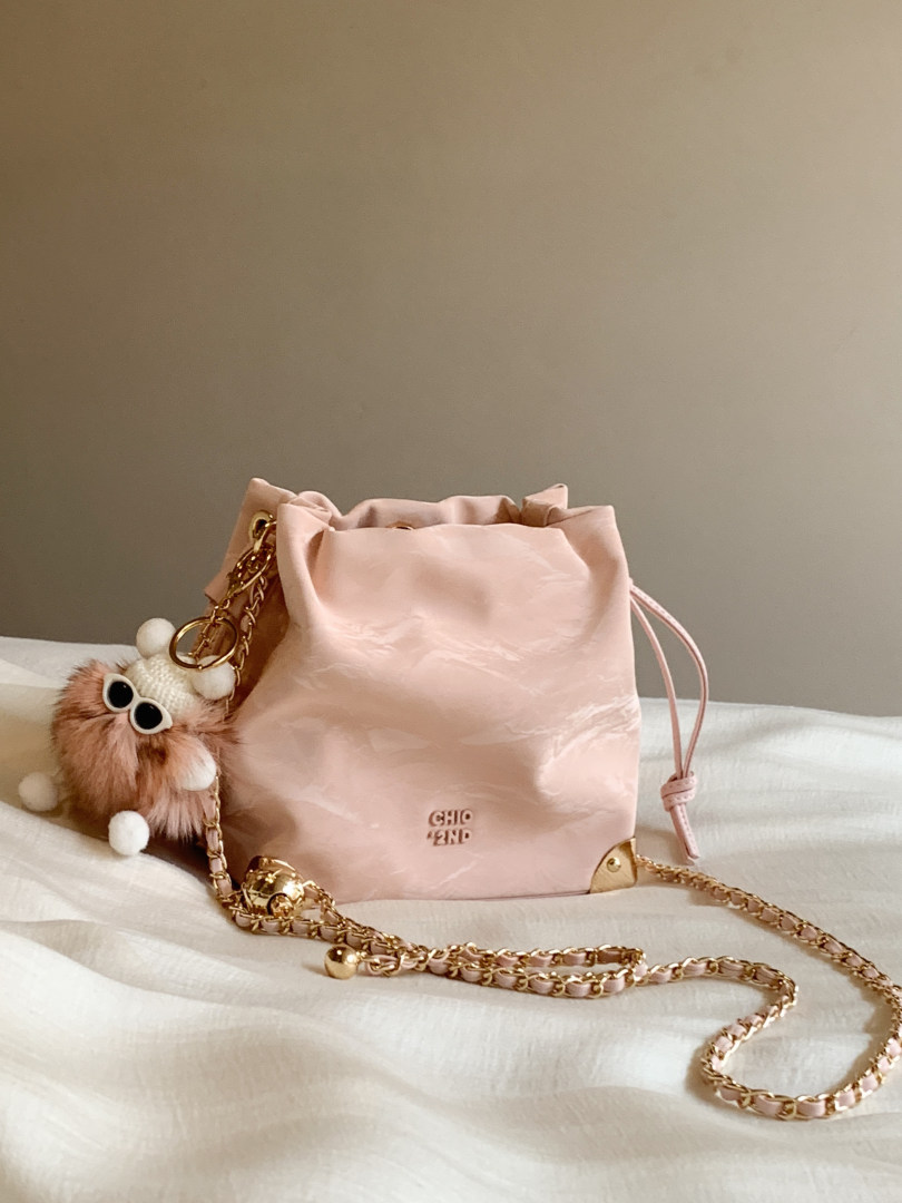 Pink drawstring handbag with gold chain strap and fluffy charm on a bed