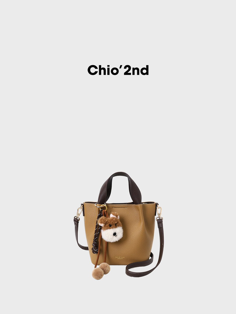 Brown leather bucket handbag with shoulder strap and plush charm on white background