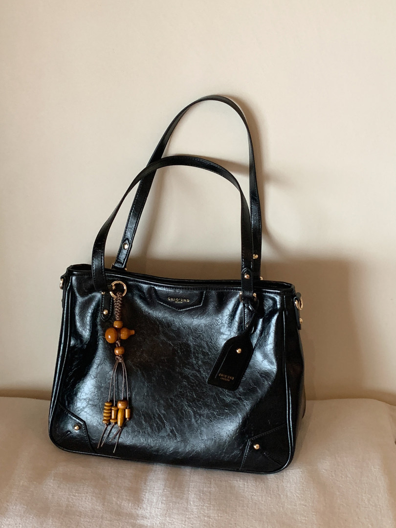 Black leather shoulder handbag with beaded charm on a neutral background