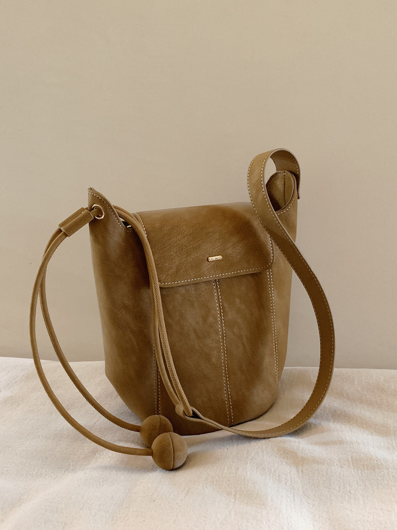 Brown leather crossbody bucket bag with long strap on a neutral background