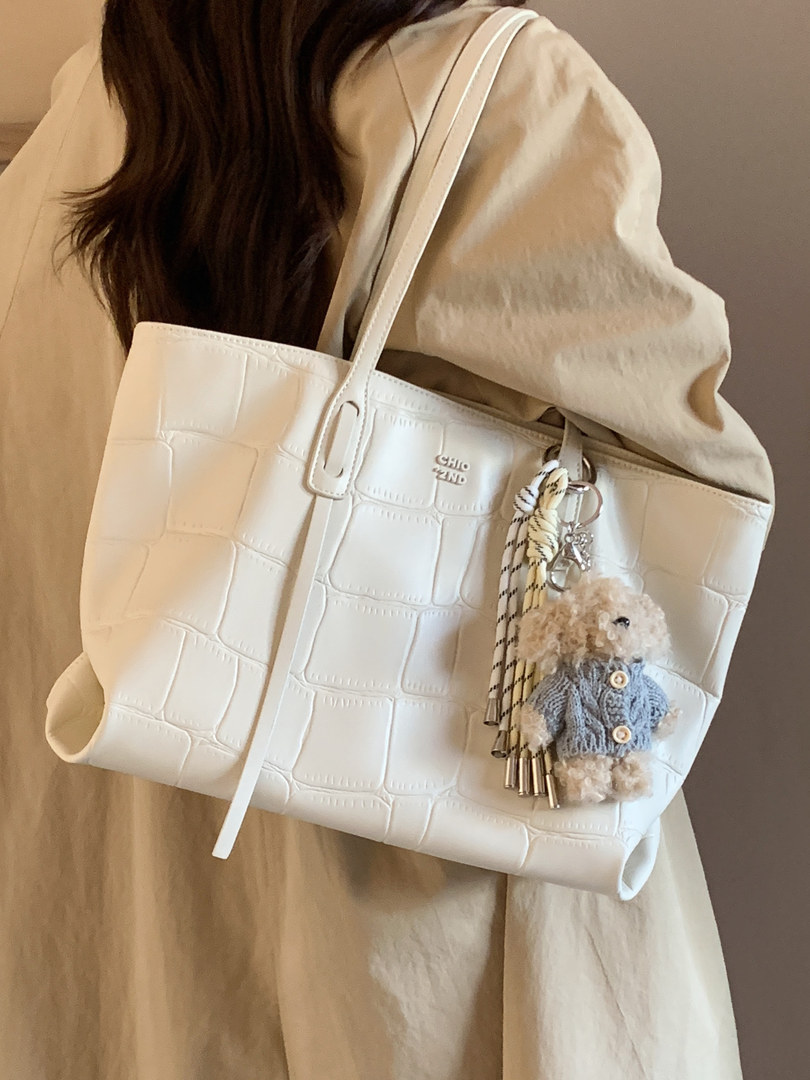 White crocodile-texture tote bag worn on a person with a teddy keychain