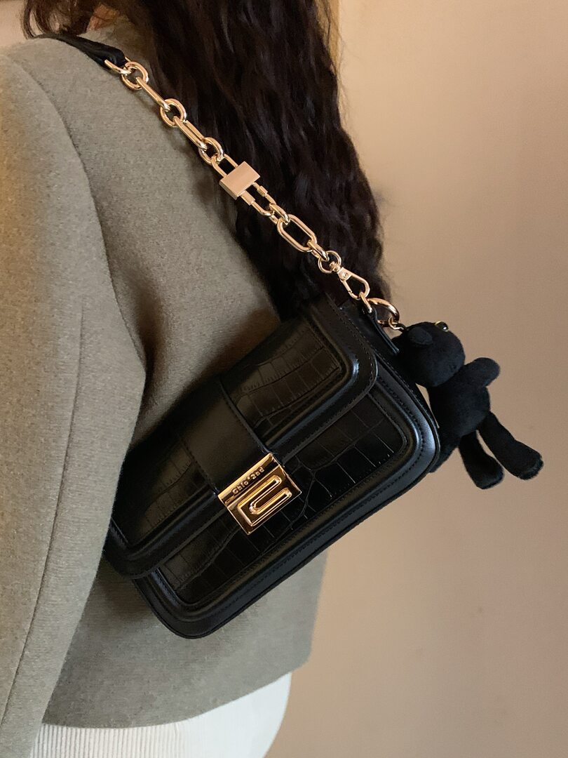 Black quilted shoulder bag with gold chain strap worn crossbody