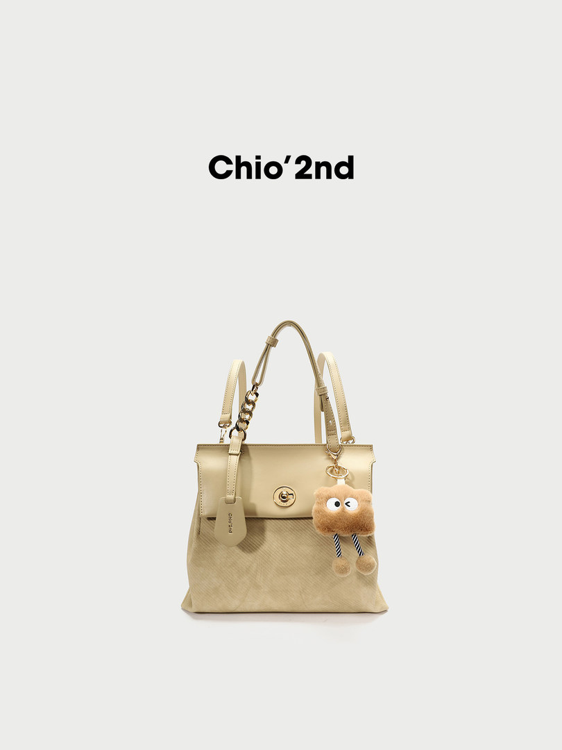 Beige handbag with shoulder straps and a fuzzy charm on a white background