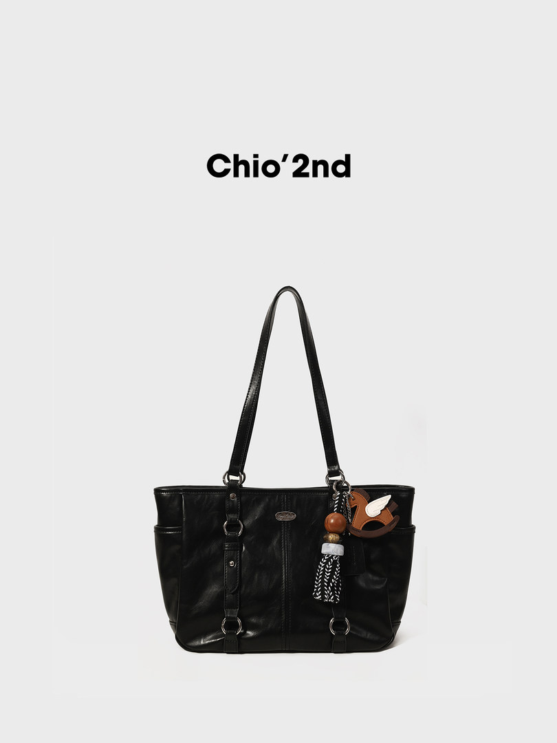 Black leather tote handbag with long shoulder straps and decorative charm on a white background