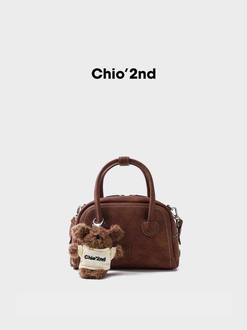 Brown handbag with a teddy bear charm on a white background
