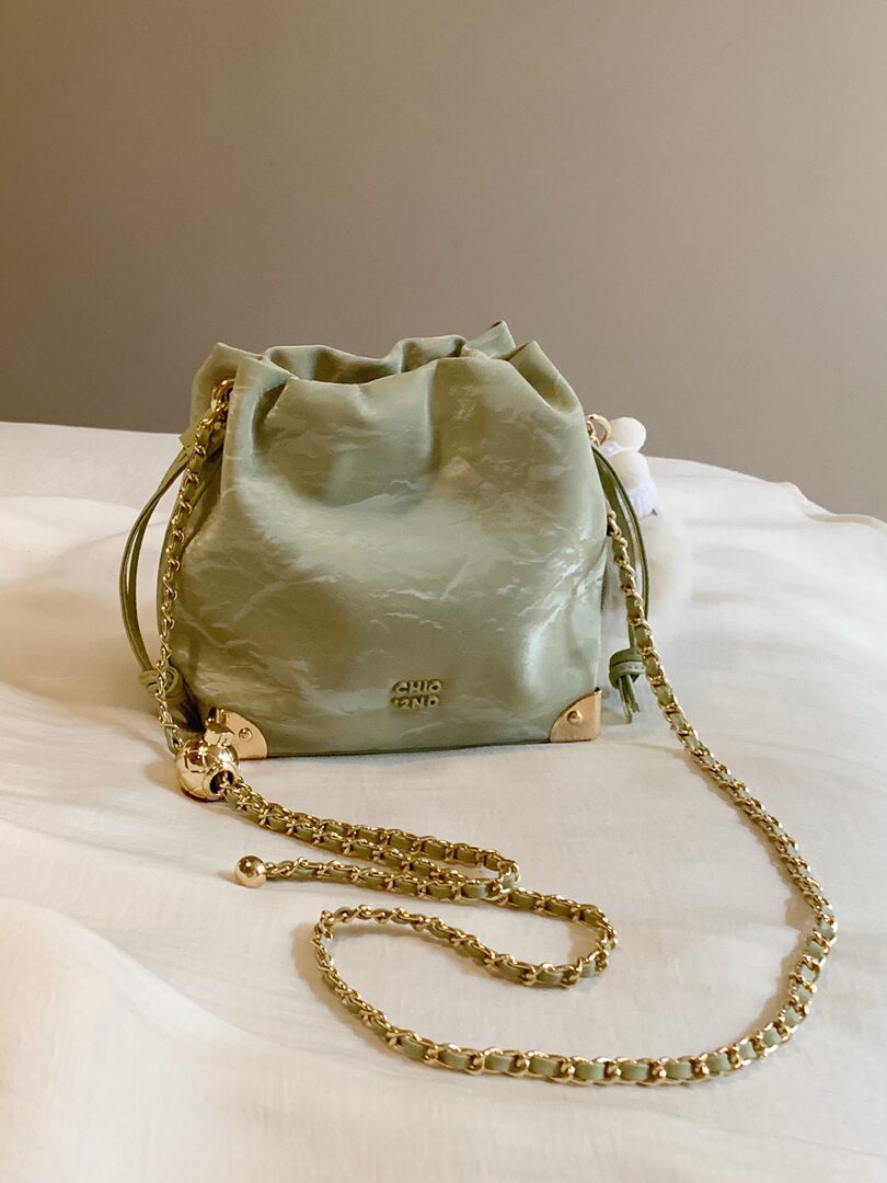 Olive green drawstring handbag with gold chain strap on a bed