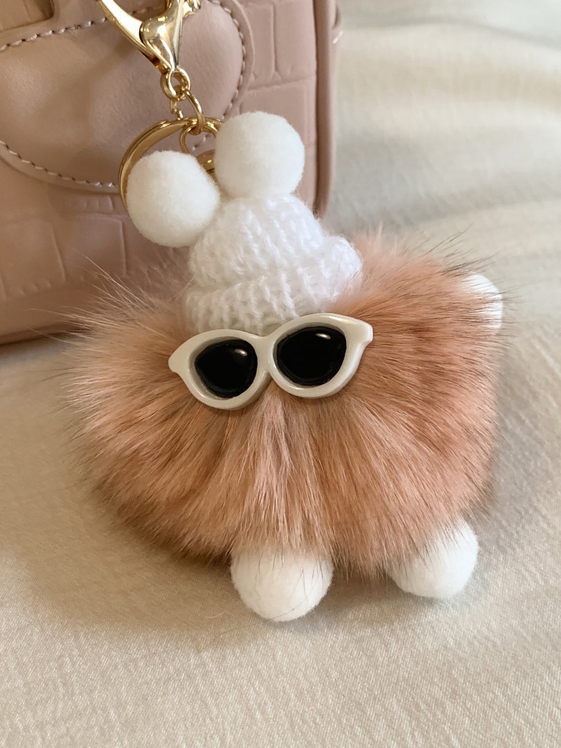 Fluffy pom-pom keychain with sunglasses charm hanging from a bag