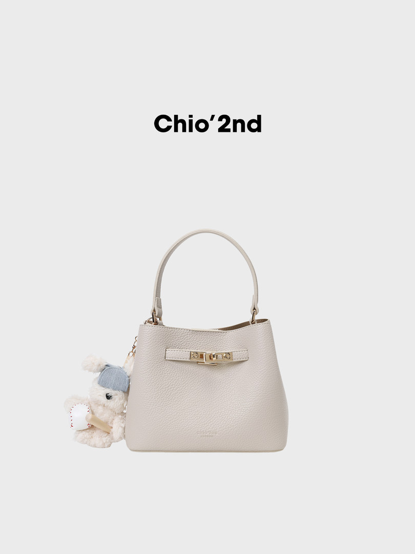 Cream leather top-handle handbag with a small teddy charm on a white background